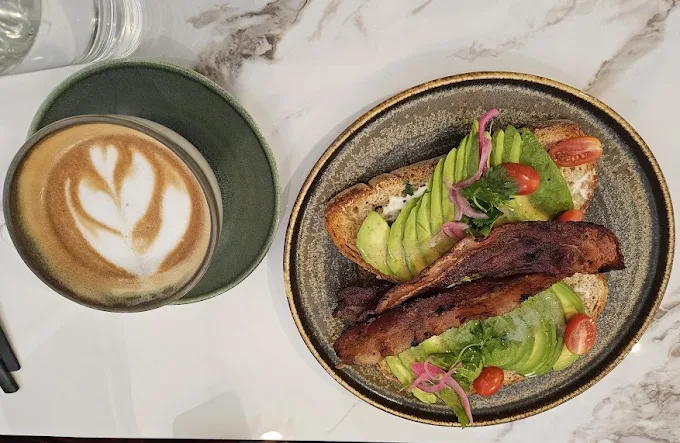 Latte art beside avocado toast with bacon